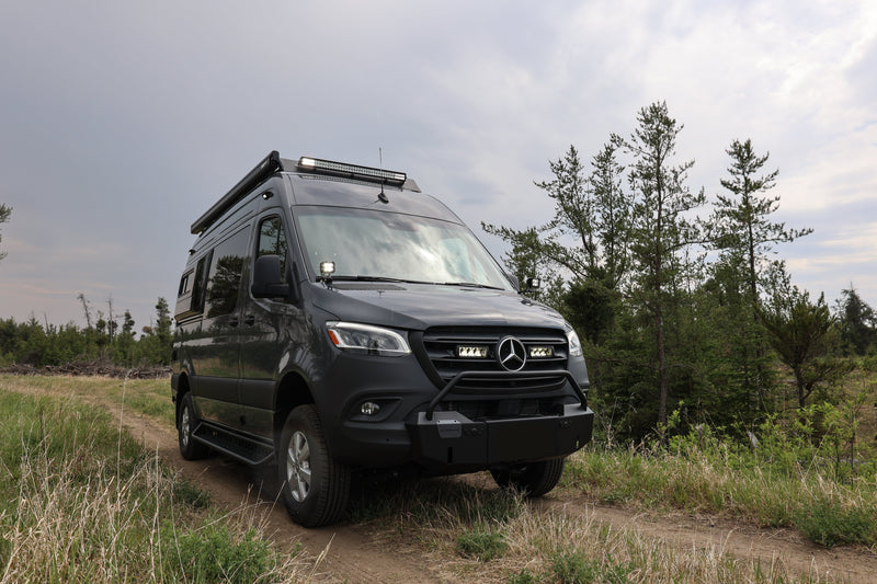 Black Mercedes-Benz van on a dirt road with trees in the background