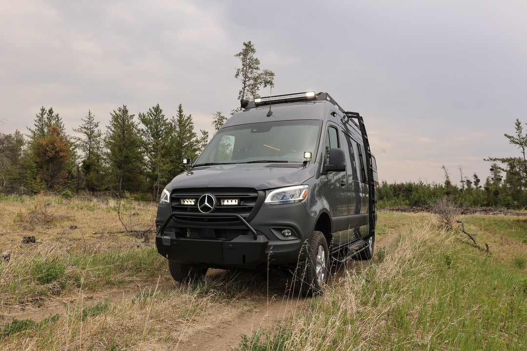 Black Mercedes-Benz van on a dirt road with trees in the background