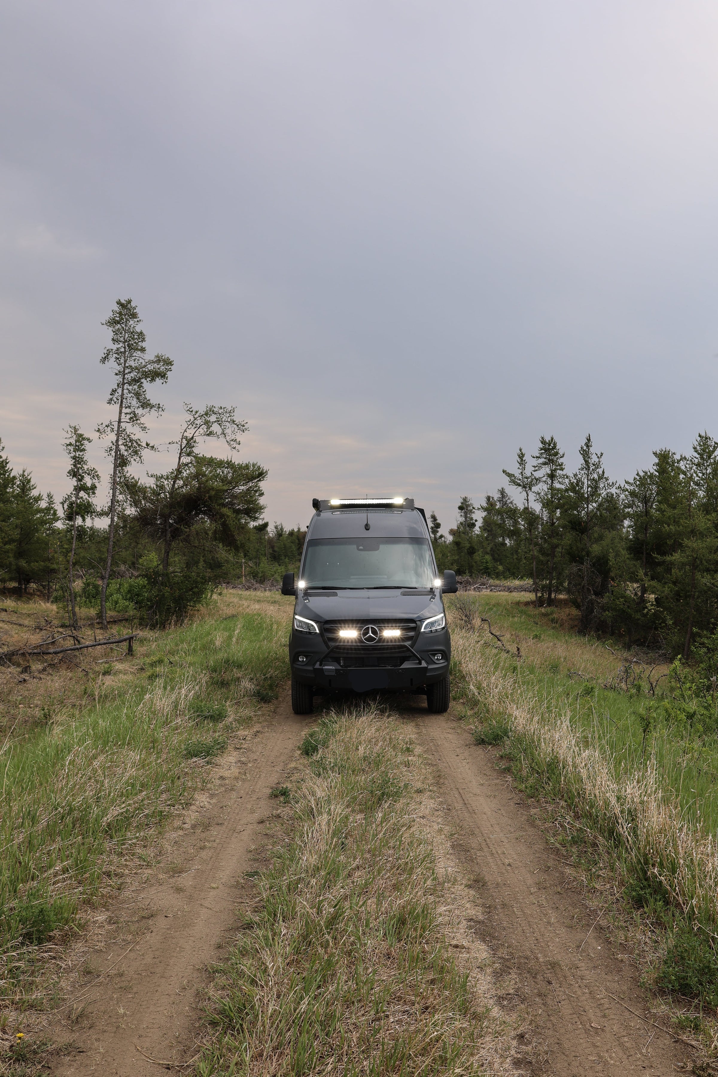 custom sprinter van conversion on a dirt road surrounded by trees under a cloudy sky